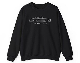 May include: A black long-sleeve sweatshirt featuring a white line art illustration of a 1973 Monte Carlo car in profile. The text 1973 MONTE CARLO is printed in white capital letters directly underneath the car graphic on the chest area.
