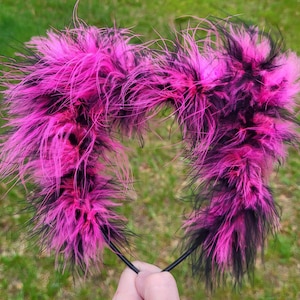 May include: Pink and black fluffy headband with a black elastic band. The headband is made of faux fur and is perfect for adding a touch of whimsy to any outfit.