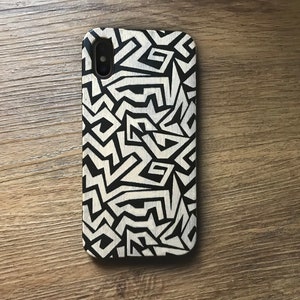 May include: A black and white phone case with a geometric pattern. The case is made of wood and has a natural finish.