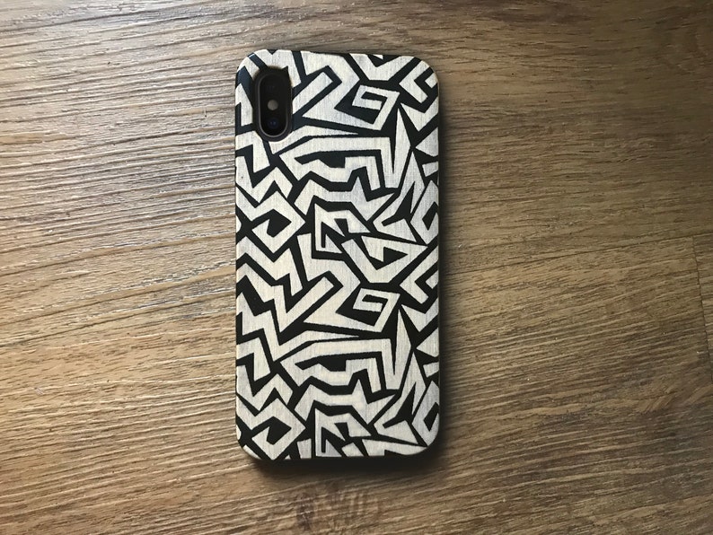 May include: A black and white phone case with a geometric pattern. The case is made of wood and has a natural finish.