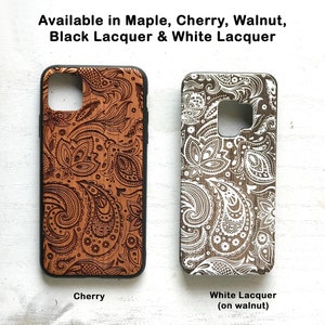 May include: Two phone cases with a paisley design. The case on the left is cherry wood with a brown paisley design. The case on the right is walnut wood with a white paisley design. The text below the cases reads "Cherry" and "White Lacquer (on walnut)".