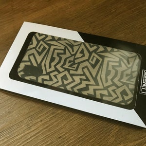 May include: A white and black phone case with a geometric pattern. The case is in a white box with a black border and the word "U'NEEK" printed on the side.