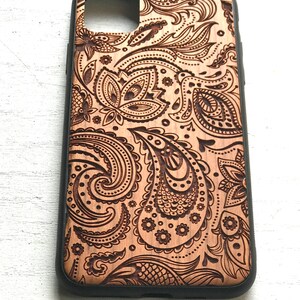 May include: A wooden phone case with a paisley pattern carved into the surface. The case has a black border.
