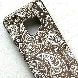 May include: A brown phone case with a white paisley pattern. The case has a cutout for the camera lens.