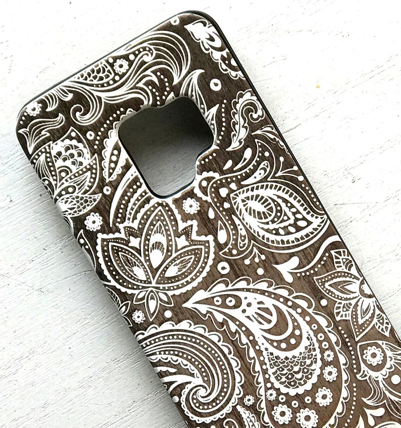 May include: A brown phone case with a white paisley pattern. The case has a cutout for the camera lens.