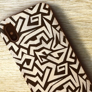 May include: A black and white geometric pattern phone case made of wood. The case has a cutout for the phone's camera.