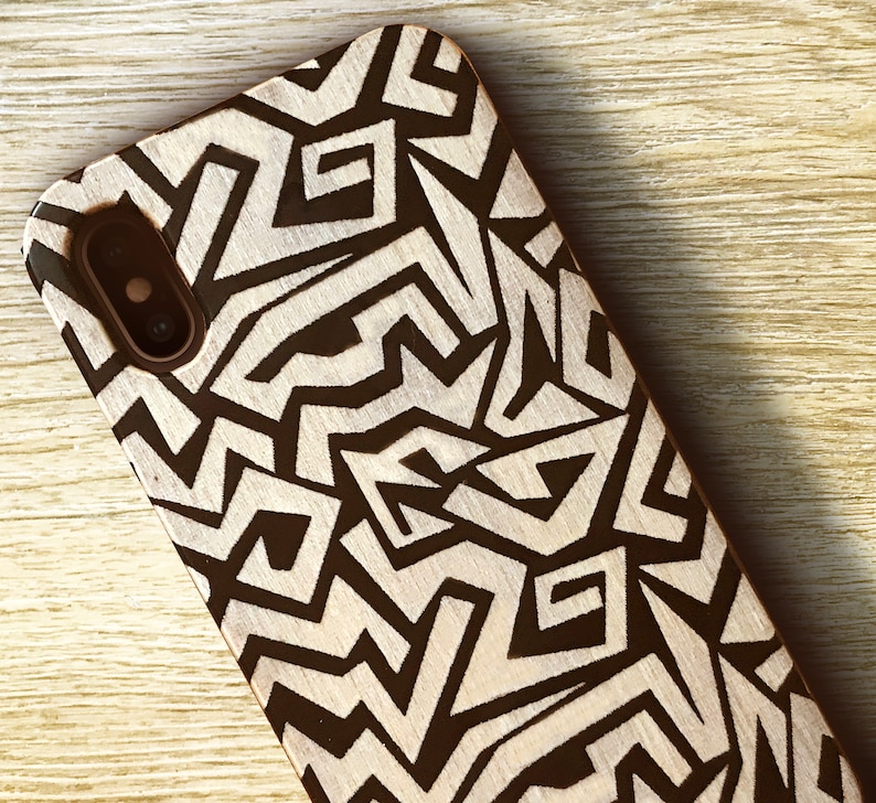 May include: A black and white geometric pattern phone case made of wood. The case has a cutout for the phone's camera.