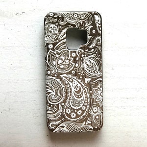 May include: A brown phone case with a white paisley pattern.