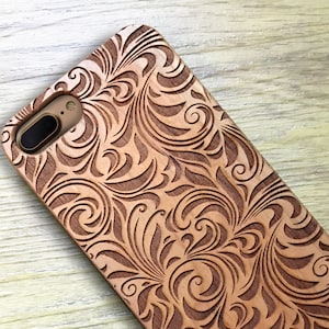 May include: A wooden phone case with a carved floral design. The case is brown and has a natural wood finish.