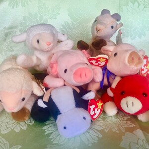 May include: A collection of seven plush toys, including a white sheep, a brown goat, a pink pig, a red bull, a white sheep, a black and white cow, and a pink pig. The toys are all Ty Beanie Babies and have their signature red and white tags.