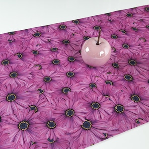 Könnte beinhalten: Ein rosa Tischläufer mit einem sich wiederholenden Muster aus rosa Blüten mit dunklen Zentren.