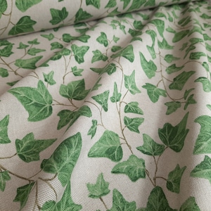 Pode incluir: Um close-up de um tecido com um padrão repetitivo de folhas de hera verdes sobre um fundo creme. O tecido é dobrado e texturizado.