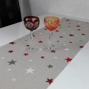 Könnte beinhalten: Zwei Kristallgläser mit Stiel und aufwendigen, geätzten Designs. Die Gläser stehen auf einem grauen Tischläufer mit einem roten und grauen Sternenmuster.