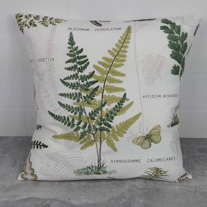Könnte beinhalten: Ein weißes Kissen mit einem botanischen Druck mit Farnen und einem Schmetterling. Das Kissen trägt den Text "Blechnum Serrulatum", "Aspidium Nevadense" und "Gymnogramme Calomelanos".
