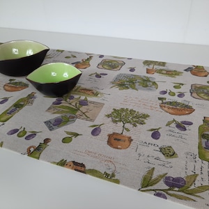 May include: A beige table runner with a repeating pattern of olive branches, olives, and bottles of olive oil. The runner has a vintage, rustic look and features handwritten text in French. Two small green and brown bowls are on the runner.