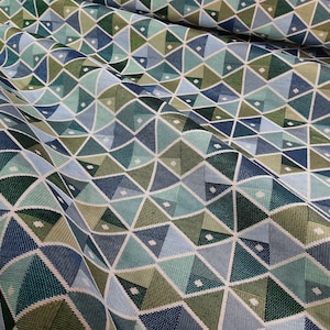 Op de afbeelding: Een stof met een geometrisch patroon van blauwe, groene en witte driehoeken. De stof is geweven met een textuur.