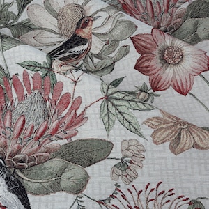 Könnte beinhalten: Ein weißer Stoff mit einem floralen Muster mit roten, rosa und grünen Blumen, Blättern und Vögeln. Der Stoff hat eine gewebte Textur.