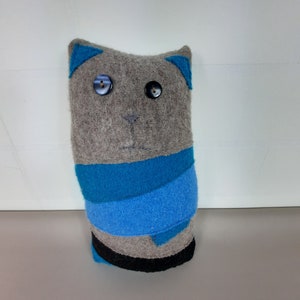 Könnte beinhalten: Ein graues Filzkatzenspielzeug mit blauen Filzohren und einem blauen Filzschal. Die Katze hat schwarze Knopfaugen.