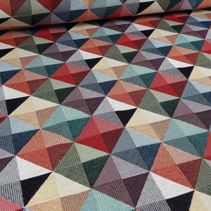 Op de afbeelding: Een kleurrijke stof met een geometrisch patroon van overlappende driehoeken in tinten rood, blauw, groen en beige.