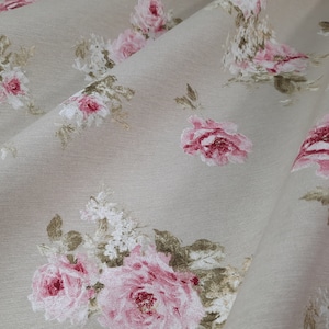 Op de afbeelding: Beige stof met een roze en wit bloemenpatroon. De stof heeft een herhalend patroon van rozen en bladeren.