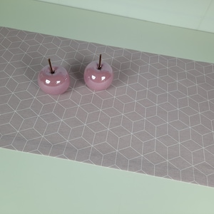 Può includere: Due mele di ceramica rosa su un runner da tavolo con motivo geometrico grigio e bianco.