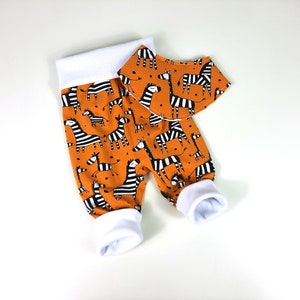 Può includere: Pantaloni da neonato arancioni e bianchi con stampa a zebre e bavaglino abbinato. I pantaloni hanno una fascia elastica bianca e polsini bianchi.