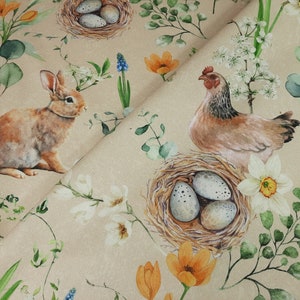 Könnte beinhalten: Ein beigefarbener Stoff mit einem sich wiederholenden Muster aus einem braunen Kaninchen, einer braunen Henne, Nestern mit Eiern, weißen Blumen und grünen Blättern.