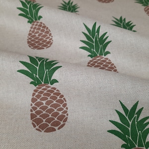 Peut inclure: Un tissu beige avec un motif répété d'ananas bruns avec des feuilles vertes.