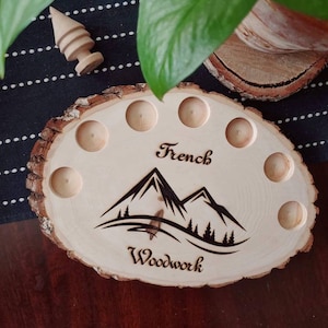 May include: A wooden tray with eight circular indentations, perfect for holding small items. The tray is decorated with a mountain scene and the words "French Woodwork".