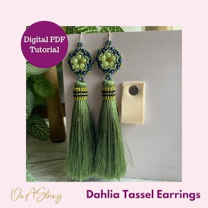 May include: Green tassel earrings with a beaded flower design. The earrings are displayed on a light purple background with the text "Dahlia Tassel Earrings" and "On A String" in the bottom corners.