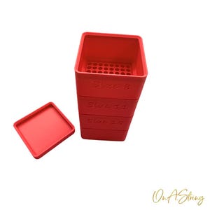 Può includere: Un contenitore rosso rettangolare con un coperchio abbinato. Il contenitore è diviso in tre sezioni, ciascuna etichettata con una dimensione: 8, 11 e 15. La sezione superiore ha una griglia di piccoli fori. Il coperchio è quadrato.