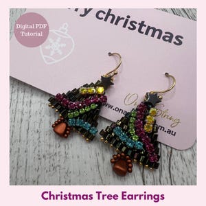 May include: A pair of Christmas tree earrings with gold hooks. The earrings are made of small, colourful beads in a tree shape, with a star at the top. The earrings are on a pink card that says "Merry Christmas".