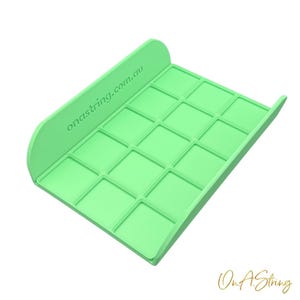 May include: A light green tray with a grid of square compartments. The tray has a curved back and sides. The text "onastring.com.au" is printed on the back. The tray is designed to hold small items.