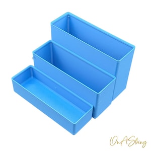 Peut inclure: Trois boîtes de rangement rectangulaires bleu clair de tailles différentes sont empilées. Les conteneurs sont vides et ont un intérieur texturé. Les conteneurs sont disposés en gradins, le plus petit étant à l'avant.