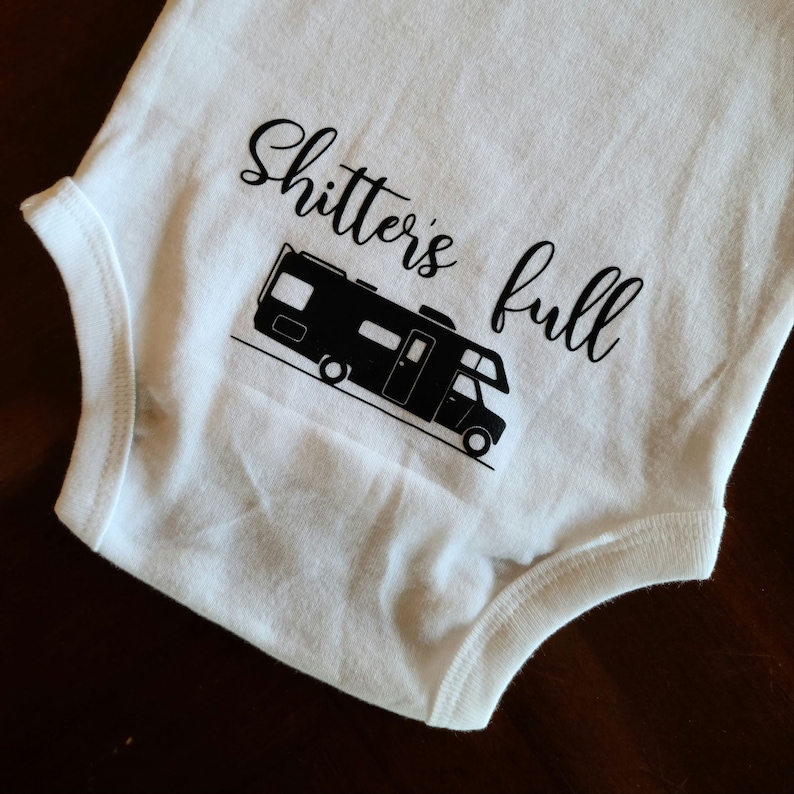 Op de afbeelding: Witte baby romper met een zwart silhouet van een camper en de tekst "Shitter's full".