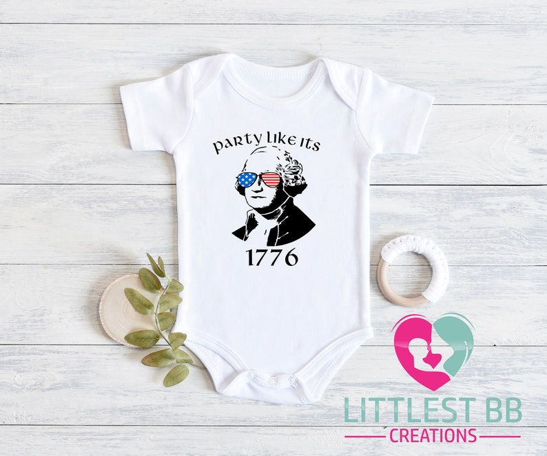 May include: White baby onesie with a graphic of George Washington wearing sunglasses with a red, white, and blue American flag design. The text "party like its 1776" is above the image, and the number "1776" is below.