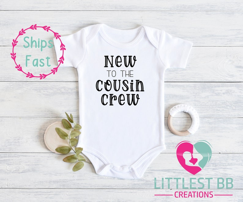 May include: White baby onesie with black text that reads "New to the cousin crew".