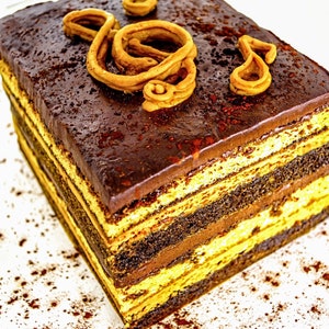 May include: A multi-layered chocolate cake with a dark chocolate ganache topping and a decorative chocolate swirl on top. The cake is sitting on a white surface with cocoa powder sprinkled around it.