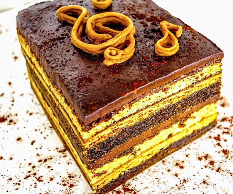 May include: A multi-layered chocolate cake with a dark chocolate ganache topping and a decorative chocolate swirl on top. The cake is sitting on a white surface with cocoa powder sprinkled around it.