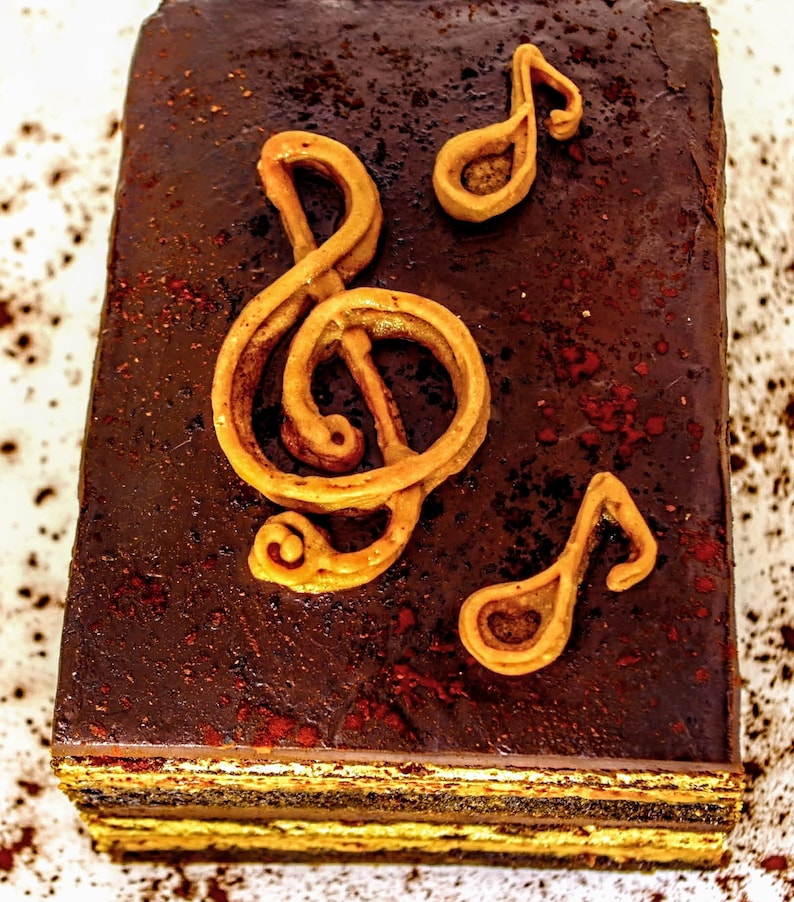 May include: A multi-layered chocolate cake decorated with brown sugar and three golden musical notes.