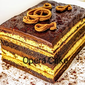 May include: A layered chocolate cake with a coffee and chocolate filling, topped with a chocolate ganache and a swirl of caramel. The cake is dusted with cocoa powder and the text "Opera Cake" is visible on the side.