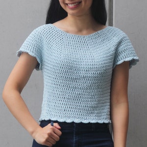 May include: A light blue crochet top with short sleeves and a scalloped hem.