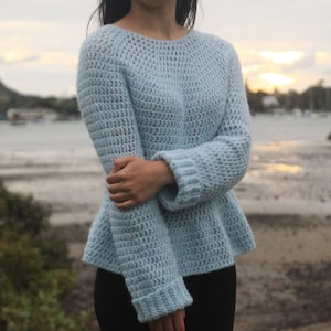 May include: A light blue crocheted sweater with a loose fit and long sleeves. The sweater has a slightly flared hemline.