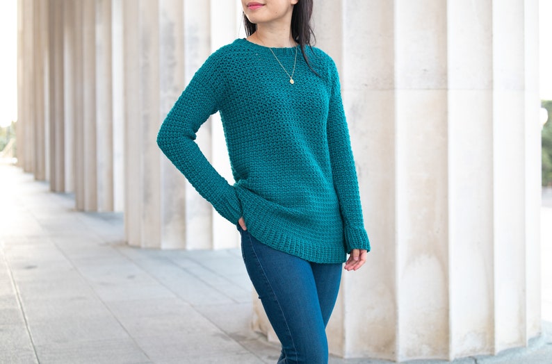 May include: A teal blue crocheted sweater with long sleeves and a round neckline.