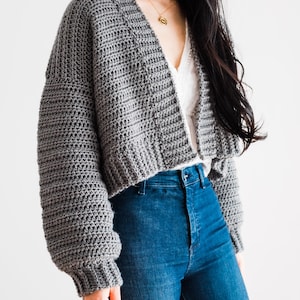 May include: A gray cropped cardigan with long sleeves and a V-neck. The cardigan is made of a soft, textured yarn.