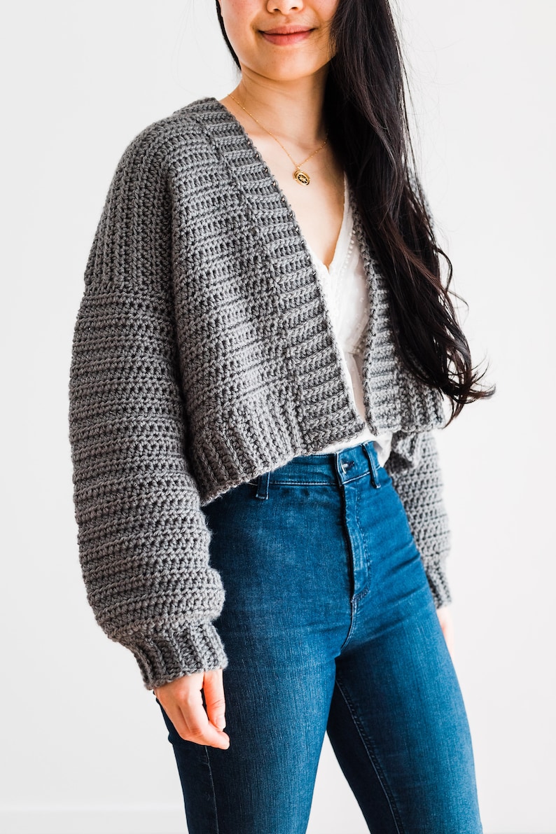 May include: A gray cropped cardigan with long sleeves and a V-neck. The cardigan is made of a soft, textured yarn.