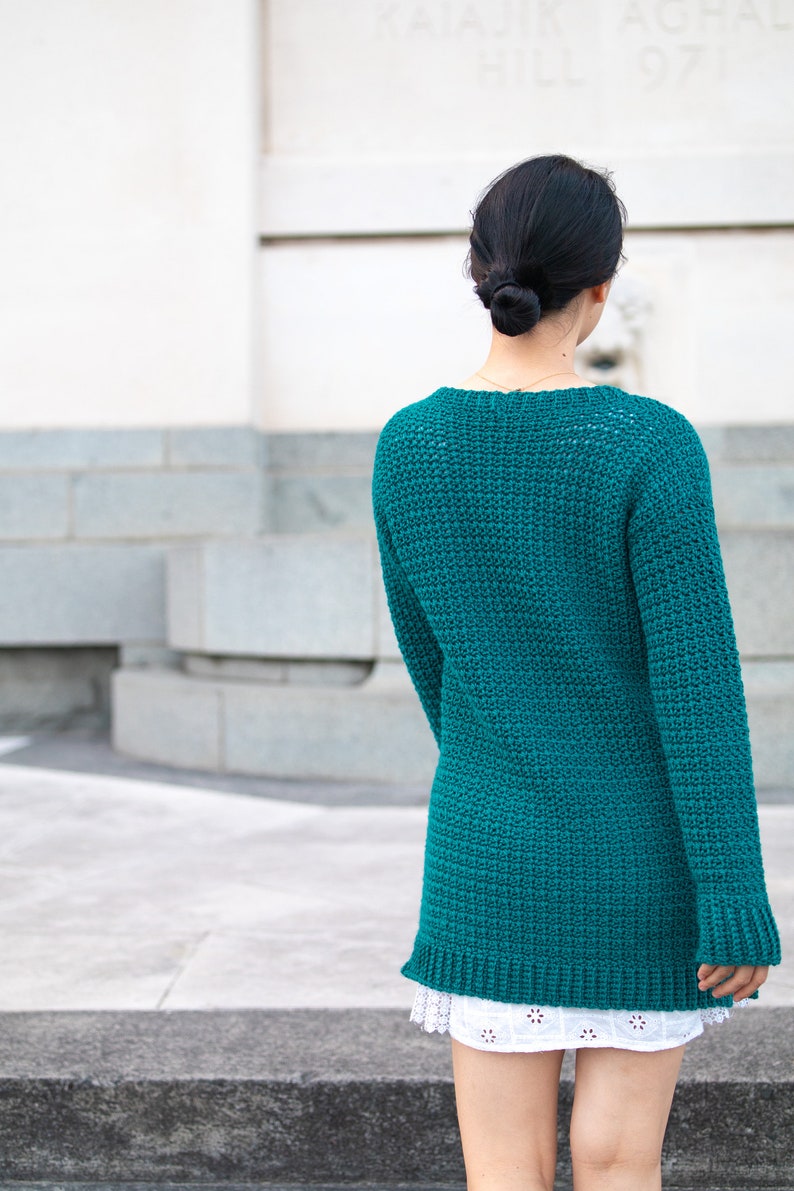 May include: A teal blue crocheted sweater with long sleeves and a loose fit.