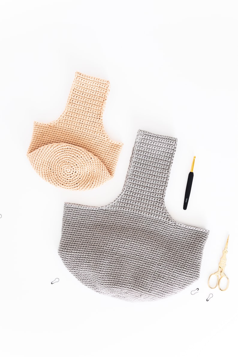 May include: Two crocheted bags, one beige and one gray, are laid out on a white surface.  A crochet hook and scissors are also pictured.
