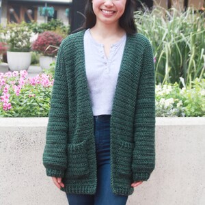May include: A dark green crocheted cardigan with pockets. The cardigan is open in the front and has long sleeves.