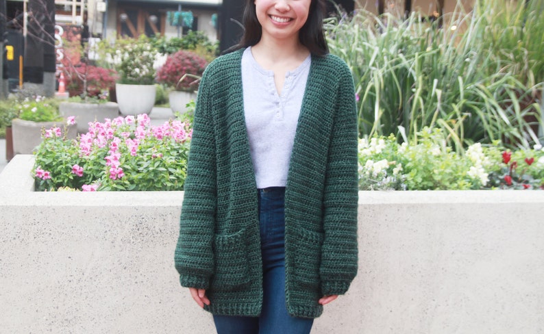 May include: A dark green crocheted cardigan with pockets. The cardigan is open in the front and has long sleeves.
